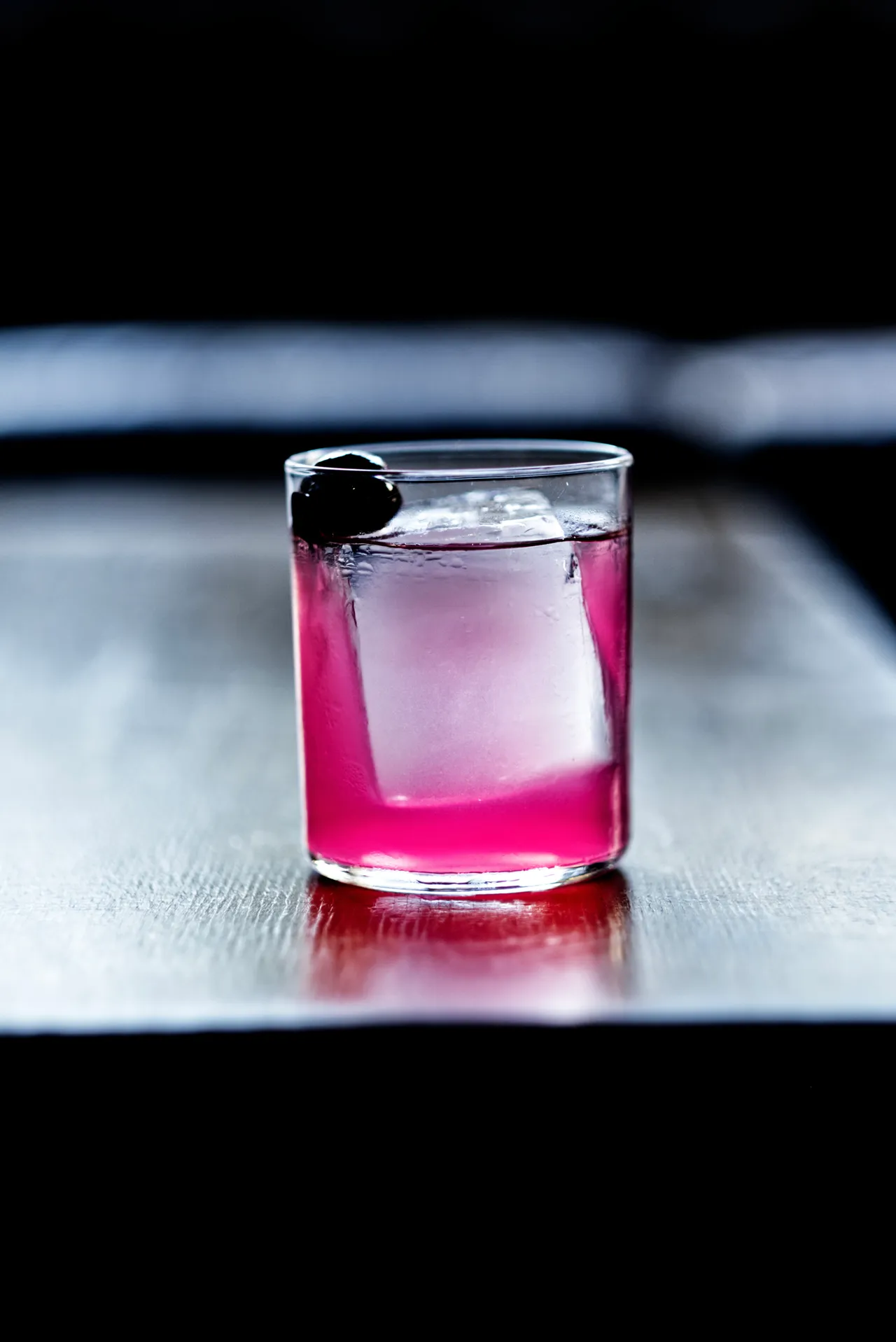 Magenta cocktail with a dark cherry on a glossy counter, pink reflection