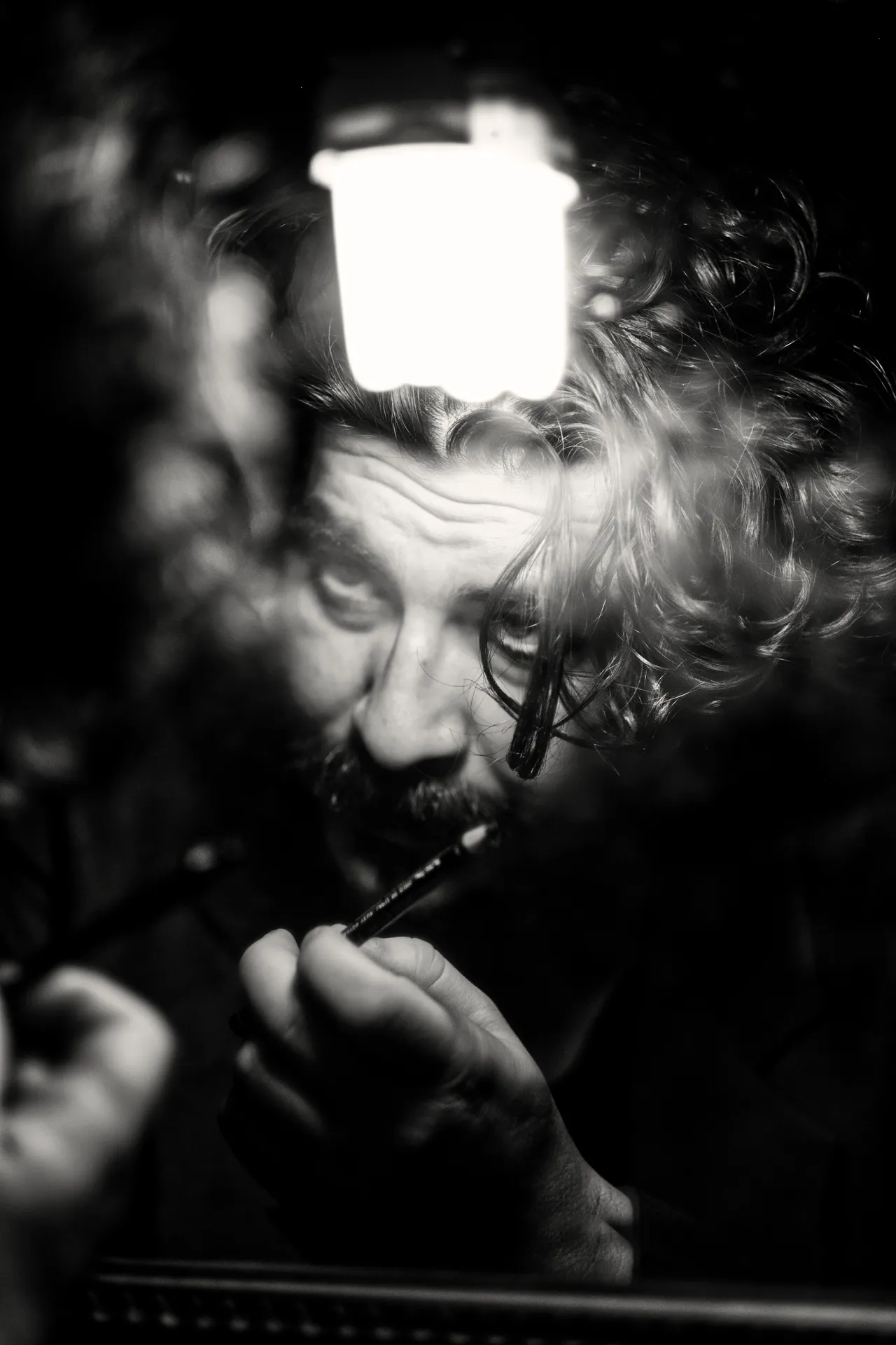 The same man in black and white, the lantern glowing above his face, a pen between his fingers
