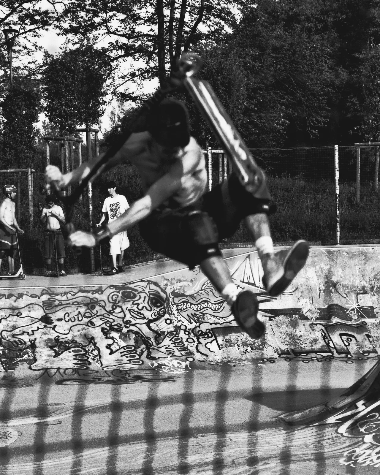 Ragazzo in salto con il monopattino sopra un muro di graffiti in uno skatepark