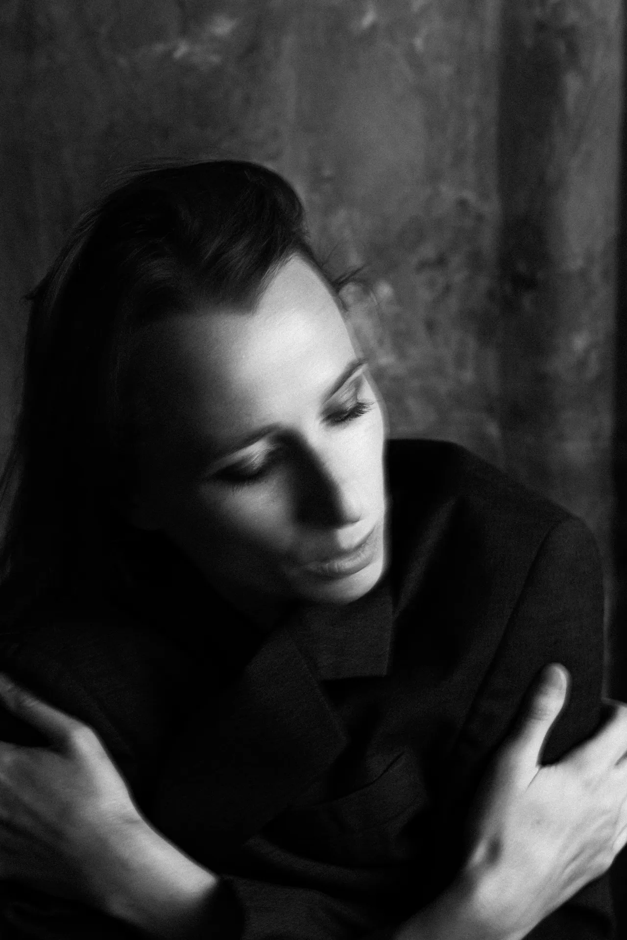 The same woman in black and white, eyes lowered, hands resting on her arms