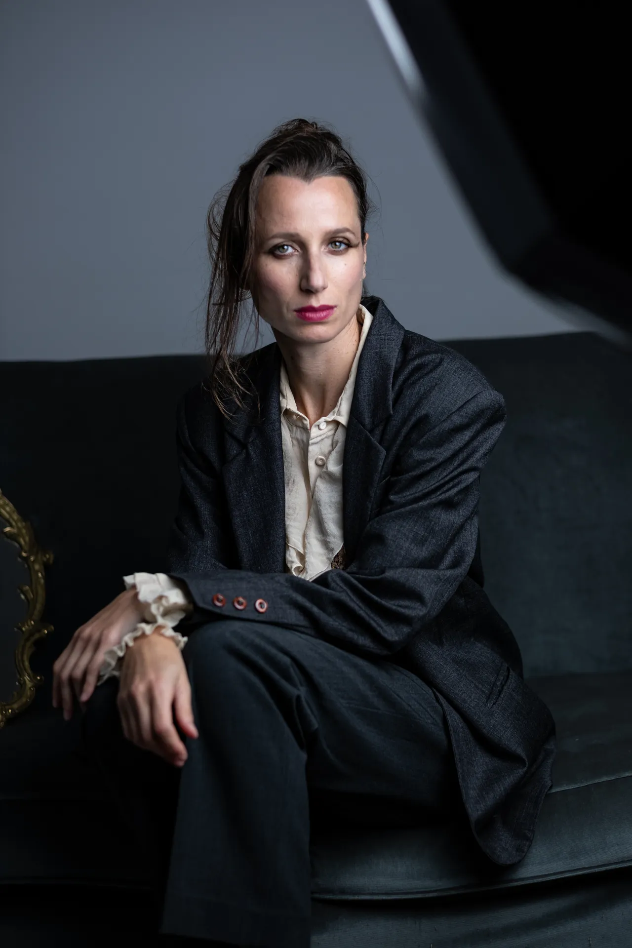 Woman in a navy blazer seated on a velvet sofa, looking straight into the camera