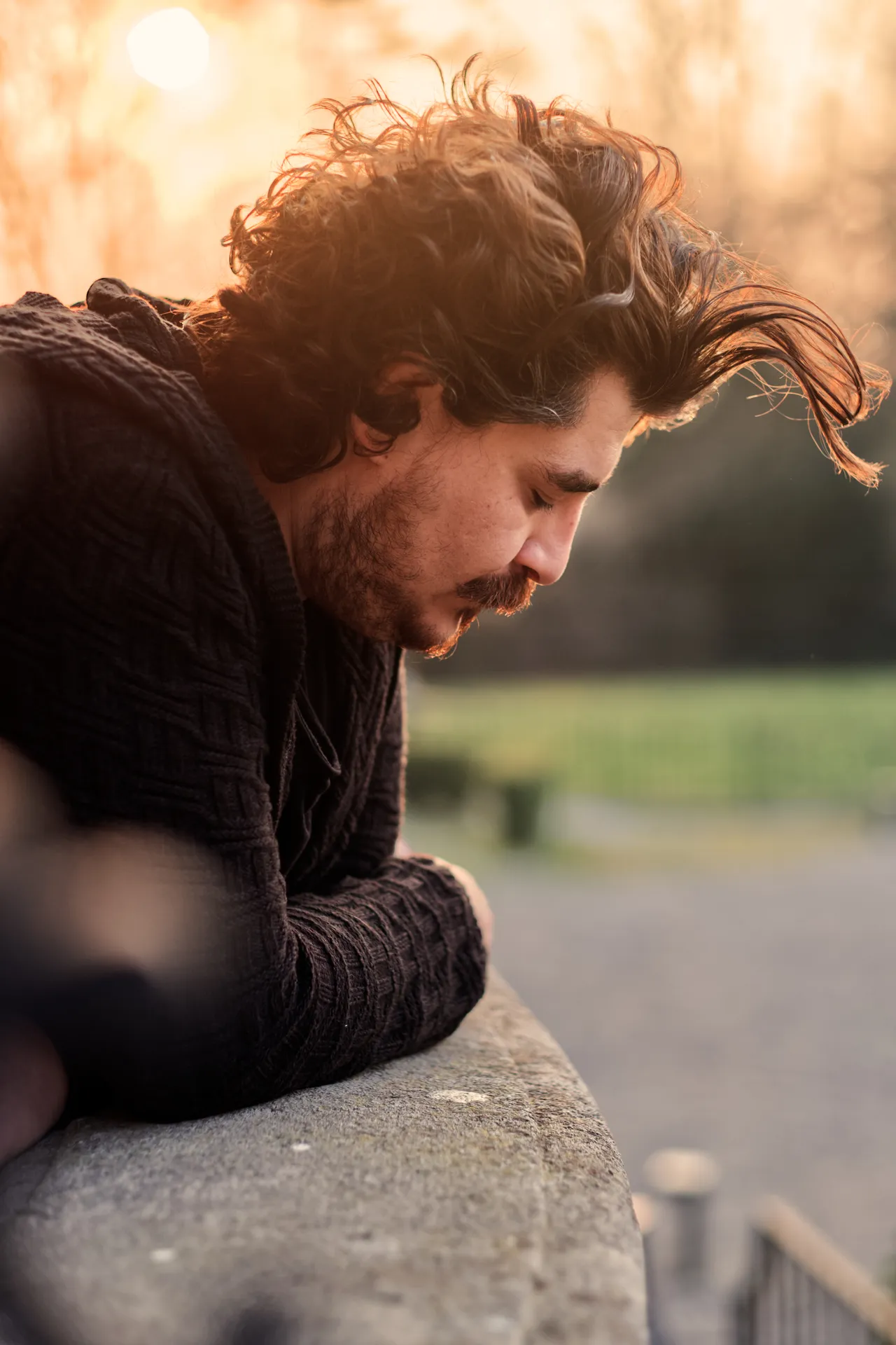 Man leaning on a low wall against the sunset, his curly hair lit by the sun