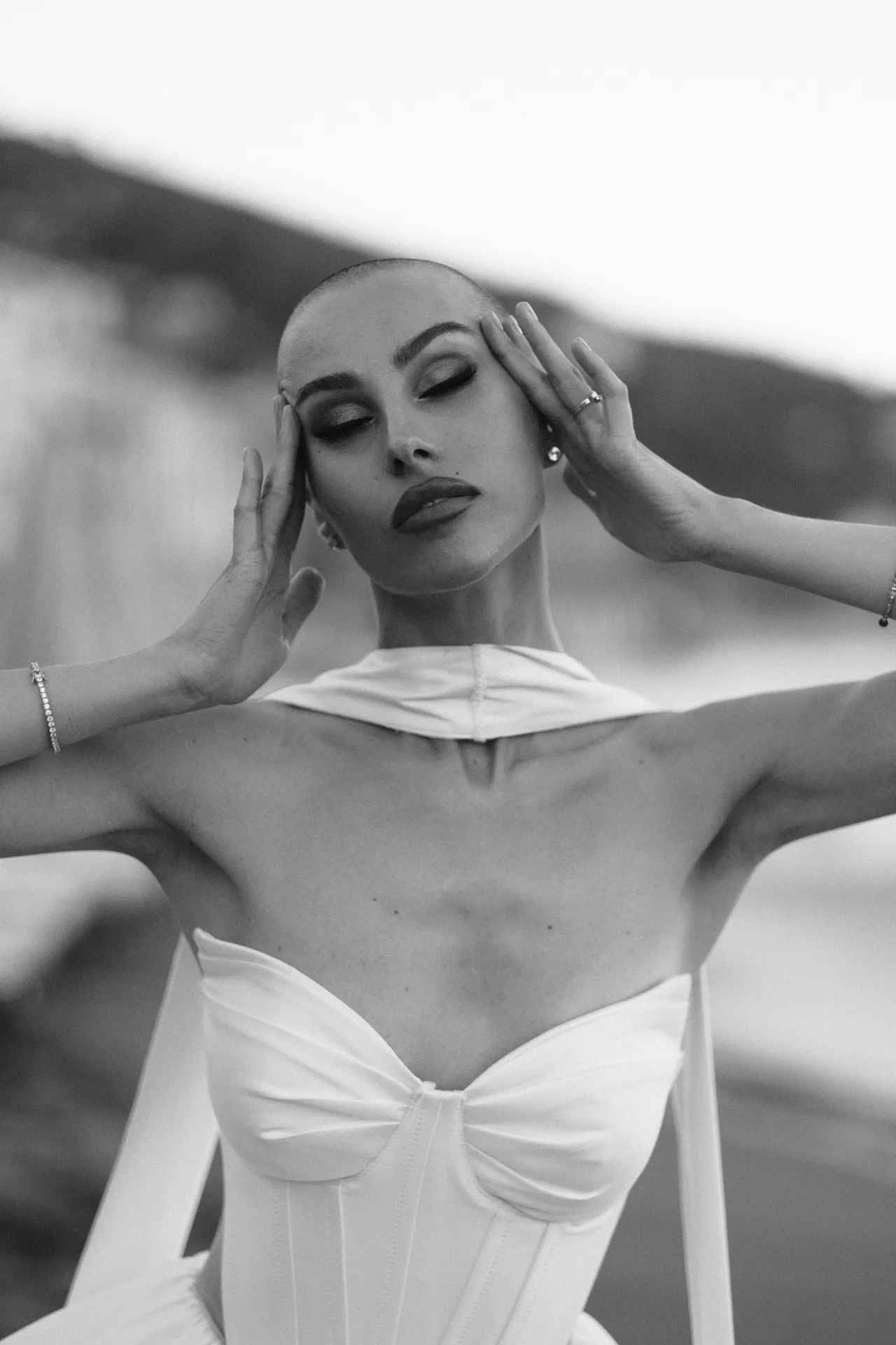 Woman with her hands at her temples and eyes half closed, in a white corset