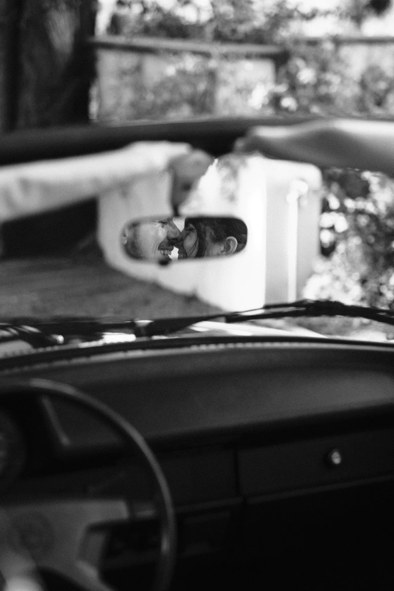 The couple reflected in a vintage car's rear-view mirror, the dashboard in the foreground