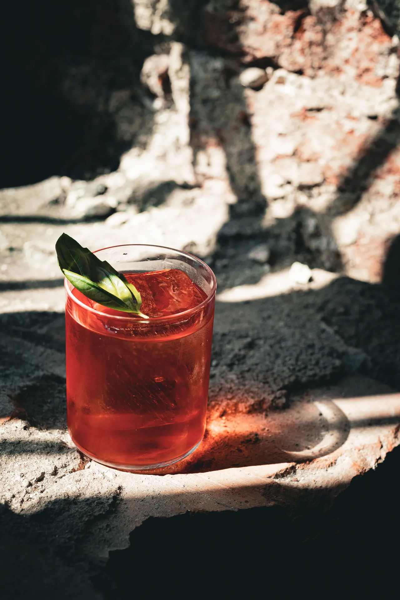 Red cocktail with a green leaf on a rough stone and brick wall