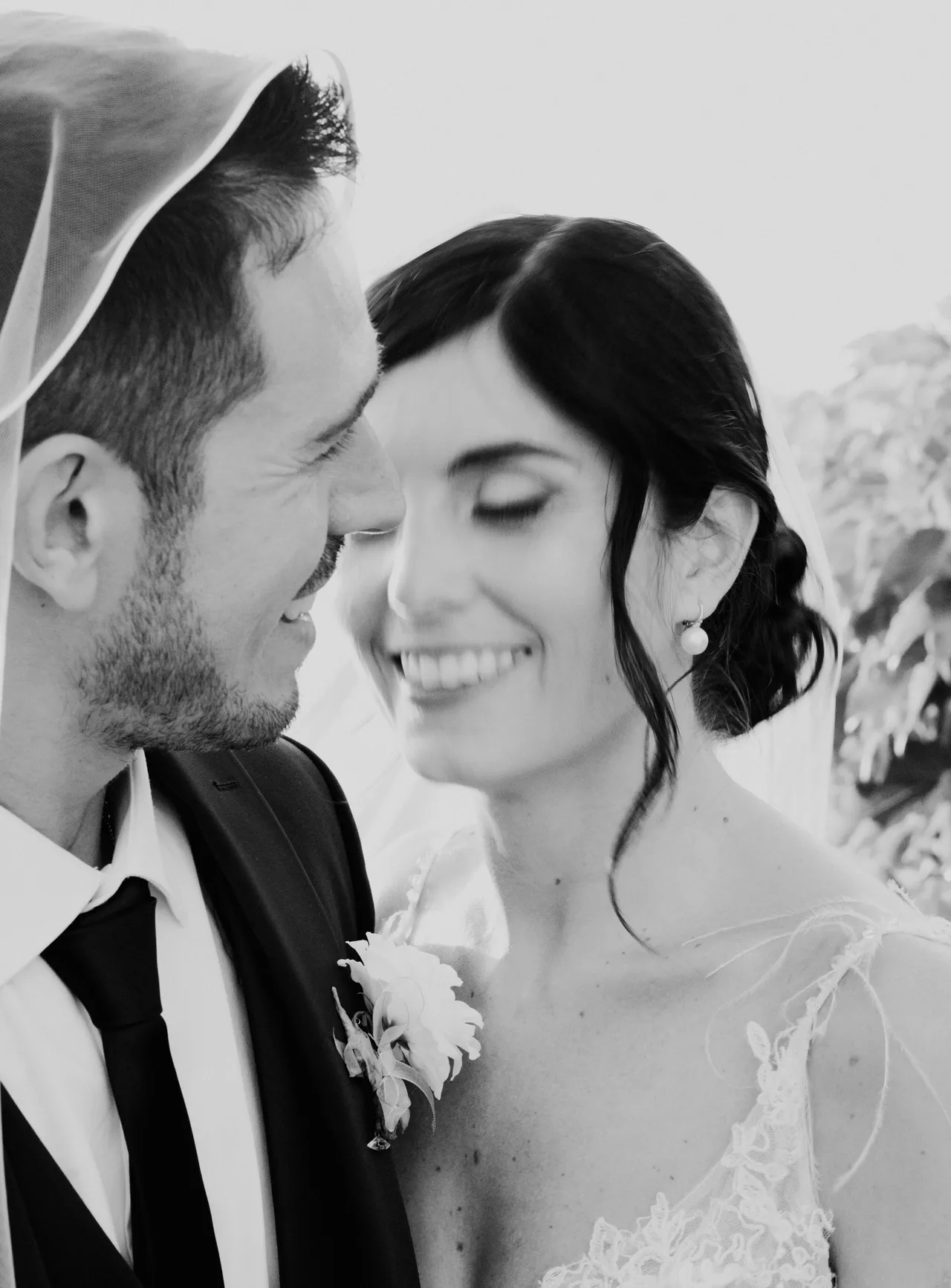 Bride and groom smiling under the same veil, cheek to cheek