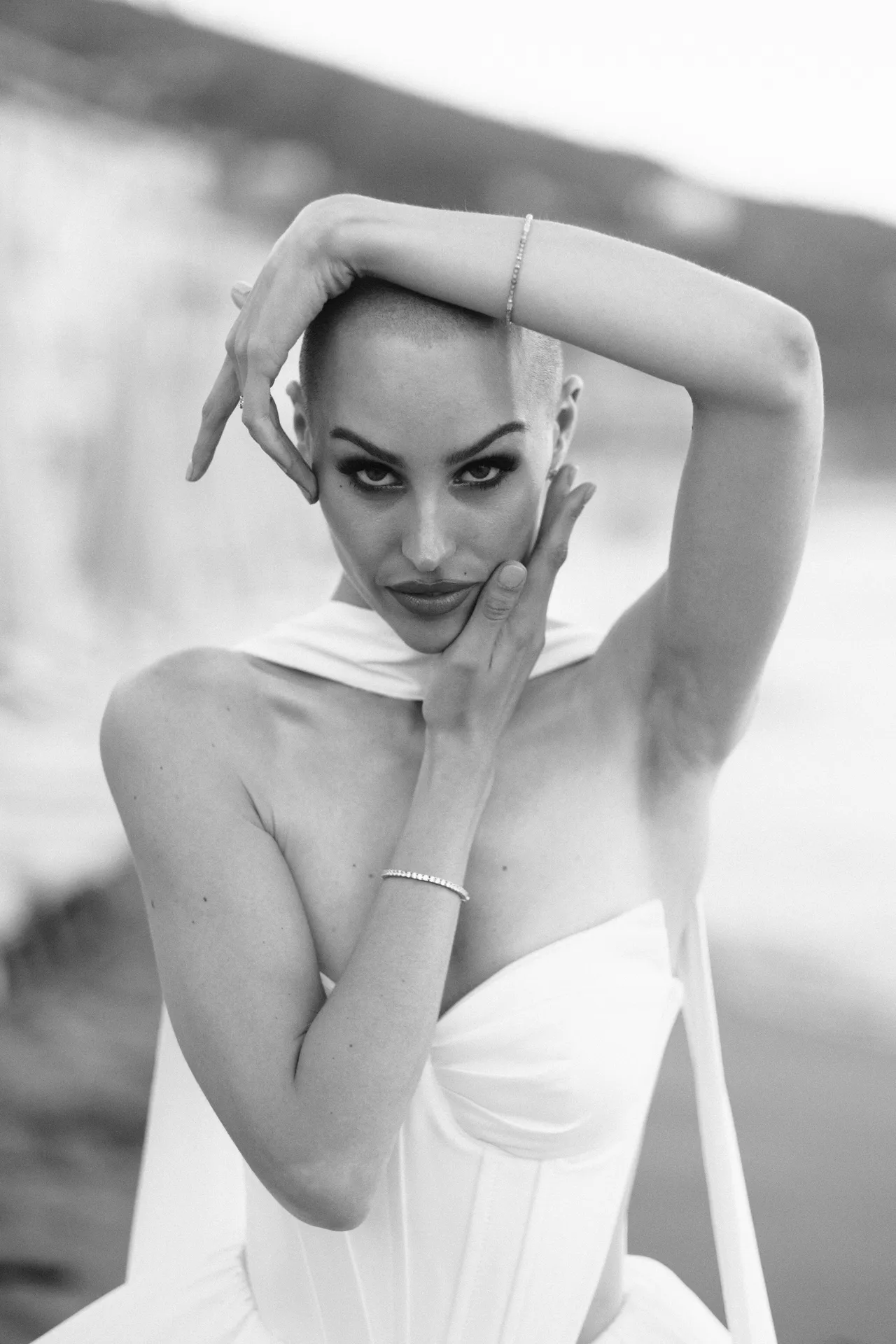 Woman with one arm bent over her head and a hand on her face, the pale coast behind