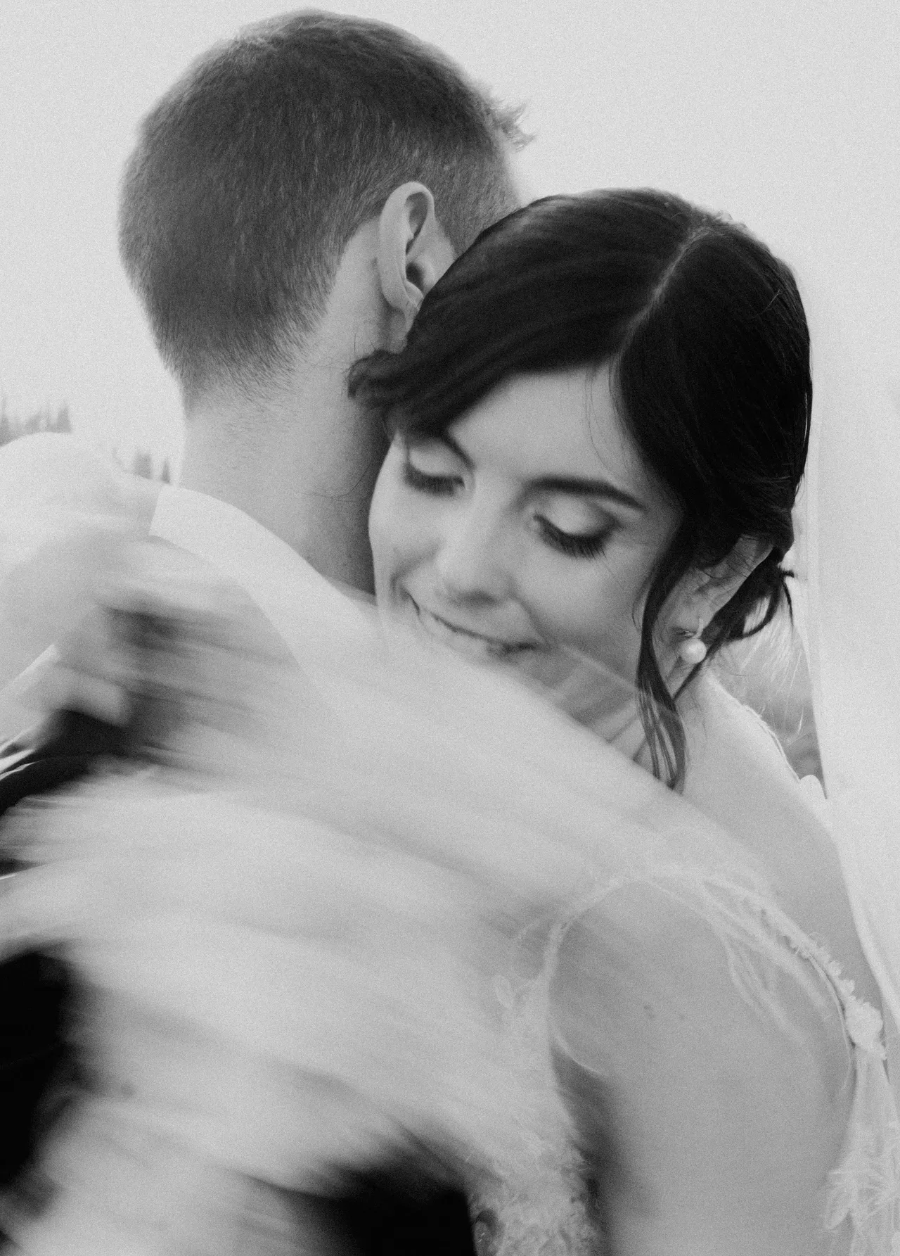Abbraccio tra gli sposi con il velo mosso dal vento, la sposa a occhi chiusi