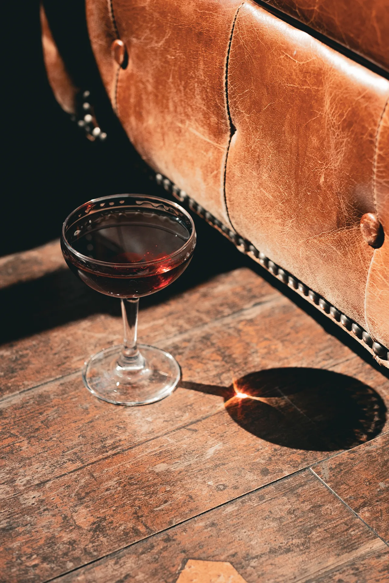 Coupette with an amber drink on wooden flooring beside a leather Chesterfield sofa