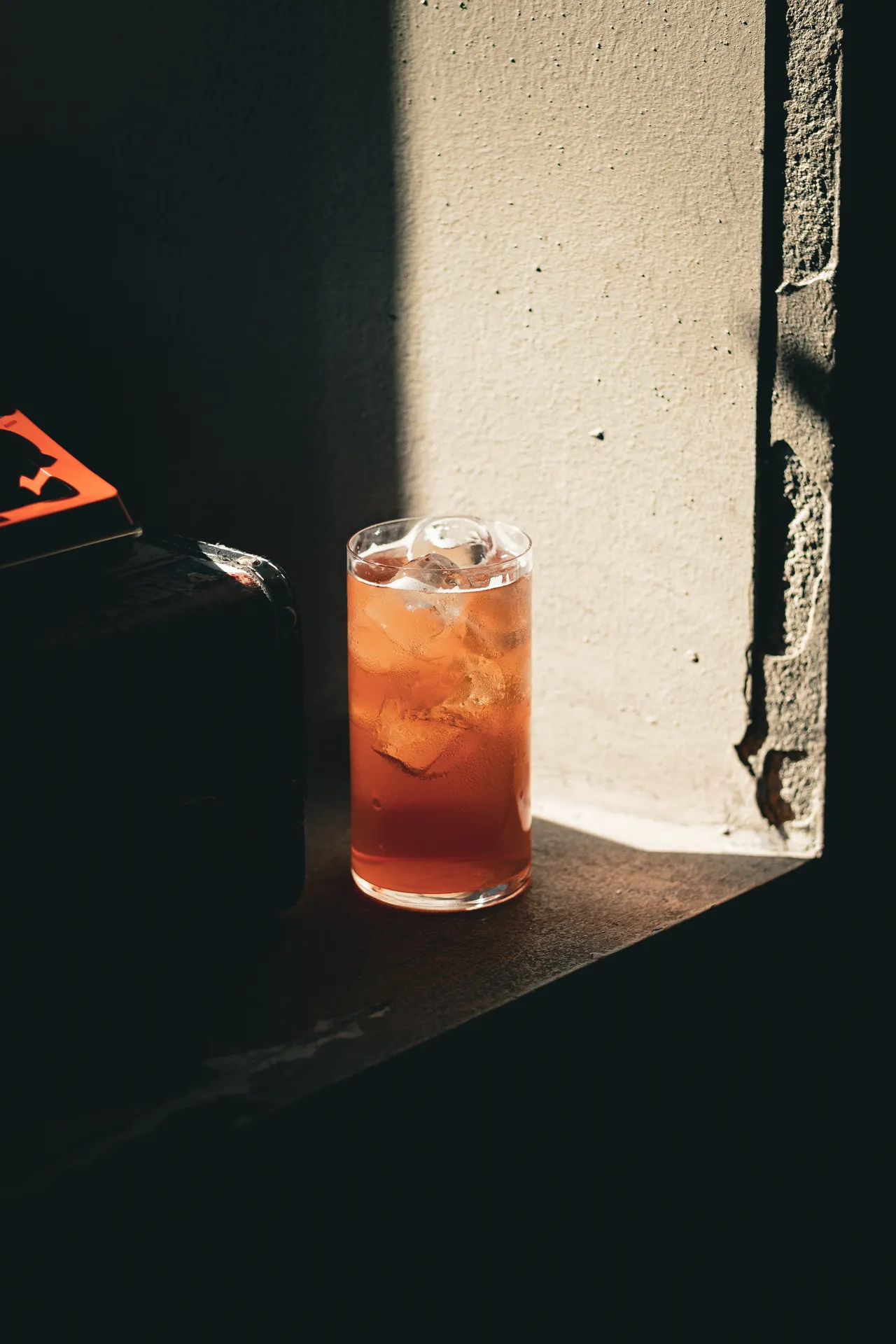 Orange highball with ice on a windowsill, half in light, half in shadow