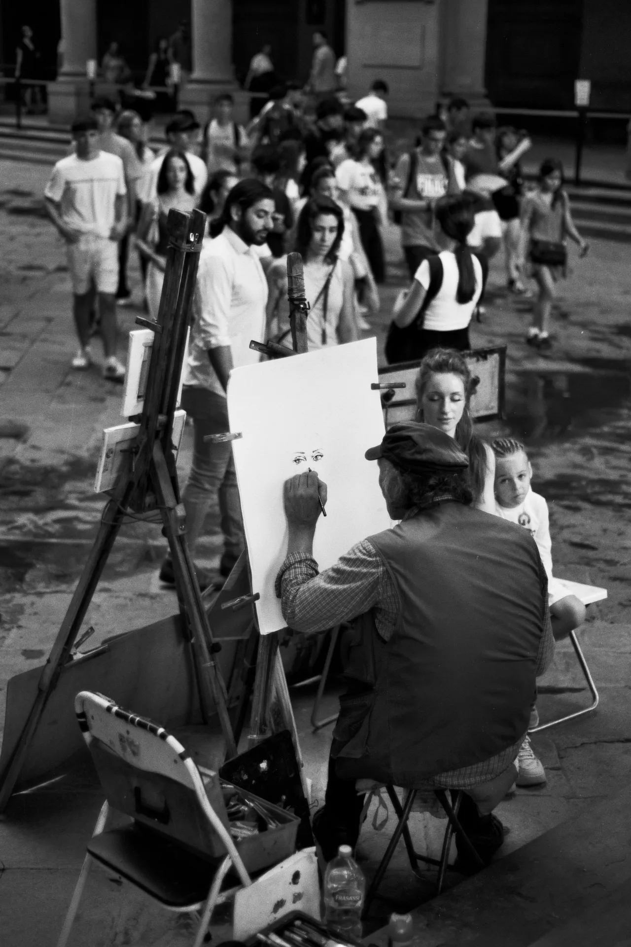 Ritrattista al cavalletto che disegna una ragazza in una piazza affollata, in bianco e nero